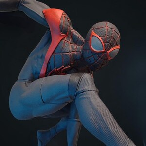 May include: A figurine of a superhero in a dynamic pose. The figure is clad in a black and blue suit with red accents on the chest and mask. The mask features red eye shapes. The figure is posed on a gray base.