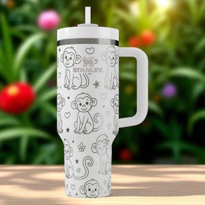 May include: White Stanley tumbler with a handle and straw, featuring a repeating pattern of cartoon monkeys, hearts, and flowers. The Stanley logo is visible. The tumbler is designed for cold beverages.