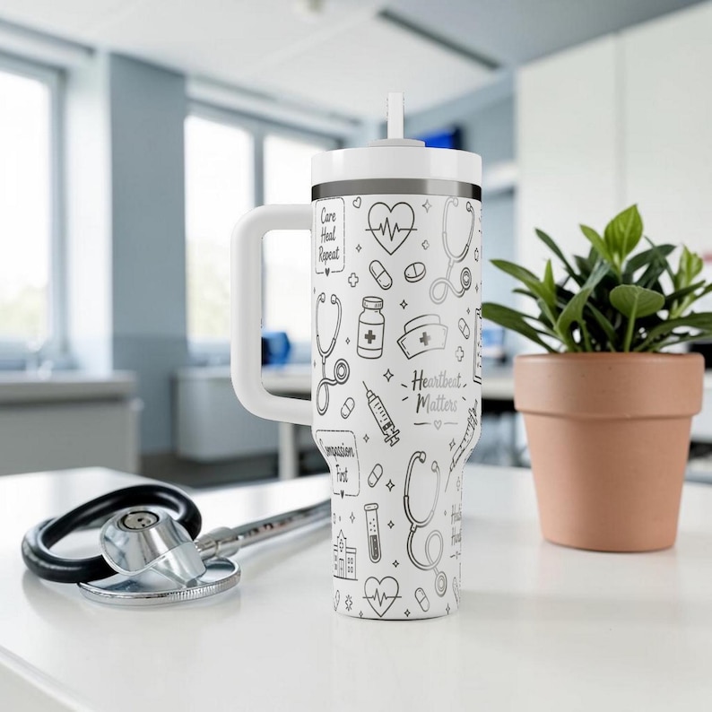 Puede incluir: Vaso blanco con asa y pajita, con un dise&ntilde;o de tem&aacute;tica m&eacute;dica. El dise&ntilde;o incluye estetoscopios, corazones, pastillas y el texto "Heartbeat Matters". Un estetoscopio descansa sobre la mesa.