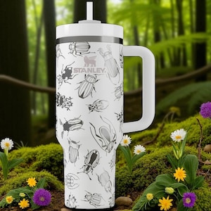 May include: A white Stanley tumbler with a handle and a straw, featuring a repeating black line art pattern of various beetle species across the exterior surface. The brand name Stanley is printed in black on the upper portion of the cup.