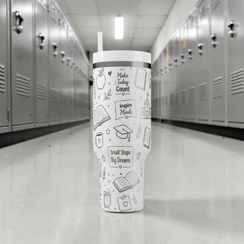 May include: A white tumbler with a black rim and a straw. The tumbler is decorated with black line drawings of an apple, books, a graduation cap, and the phrases "Make Today Count", "Inspire Minds", and "Small Steps Big Dreams".