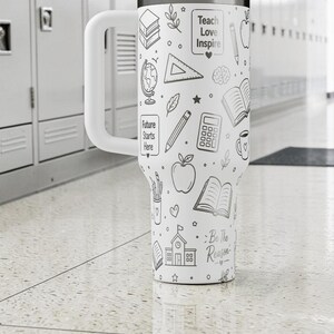 May include: White insulated tumbler with a large handle, decorated with black line art of school supplies and the phrases "Teach Love Inspire" and "Future Starts Here." The tumbler also has the phrase "Be the Reason."