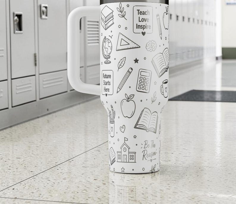 May include: White insulated tumbler with a large handle, decorated with black line art of school supplies and the phrases "Teach Love Inspire" and "Future Starts Here." The tumbler also has the phrase "Be the Reason."