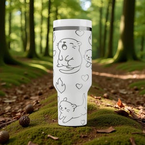 K&ouml;nnte beinhalten: Ein wei&szlig;er Becher mit einem sich wiederholenden Muster aus Cartoon-Ottern und Herzen. Der Becher hat einen wei&szlig;en Deckel und ein schwarzes Band in der N&auml;he der Oberseite. Das Design ist auf wei&szlig;em Hintergrund gedruckt. Geeignet f&uuml;r Hei&szlig;- und Kaltgetr&auml;nke.