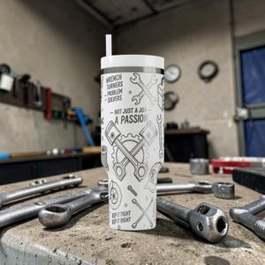 May include: A white tumbler with a black and gray design featuring wrenches, pistons, and the text "Wrench Turners - Problem Solvers - Not Just A Job - A Passion." The tumbler has a white lid and a straw. Various wrenches are scattered on the surface.