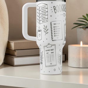 Puede incluir: Vaso blanco con un asa grande, con ilustraciones en negro de elementos de contabilidad. Incluye texto: "BOOKKEEPER", "RECEIPTS", "INVOICES", "EXPENSES", "PAYROLL", "TAXES", "DAILY PLAN" y "BALANCE SHEET".