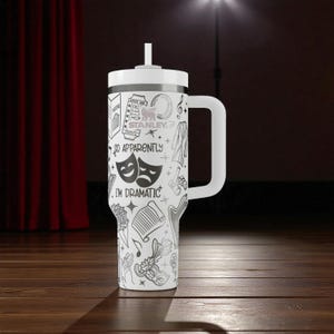 May include: White tumbler with a handle and a white lid, featuring a black and white theatrical design. The design includes drama masks, musical notes, and the text "SO APPARENTLY I'M DRAMATIC."