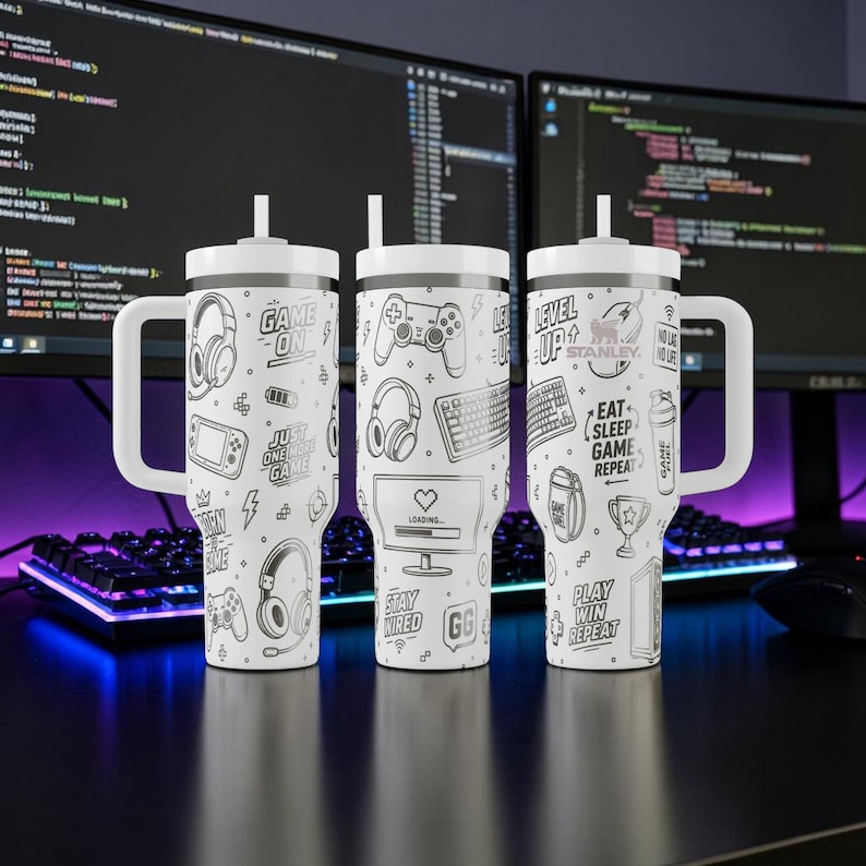 May include: Three white insulated tumblers with black gaming-themed graphics, including headphones, controllers, and keyboards. Each tumbler has a white handle and straw. Text includes "GAME ON", "LEVEL UP", "EAT SLEEP GAME REPEAT", "STAY WIRED", and "GG".