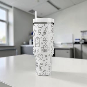Puede incluir: Vaso blanco con un dise&ntilde;o m&eacute;dico en blanco y negro. El vaso presenta ilustraciones de herramientas m&eacute;dicas, un coraz&oacute;n y el texto "Saving Lives Daily" y "Trust The Process". Incluye tapa y pajita blancas.