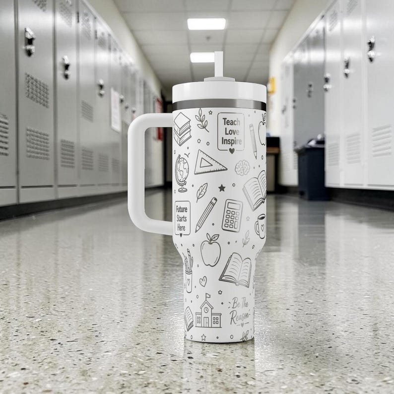 May include: A white insulated tumbler with a handle and a straw. The tumbler is decorated with black line drawings of school-related items, including books, apples, and pencils. The text "Teach Love Inspire" and "Future Starts Here" are also visible.