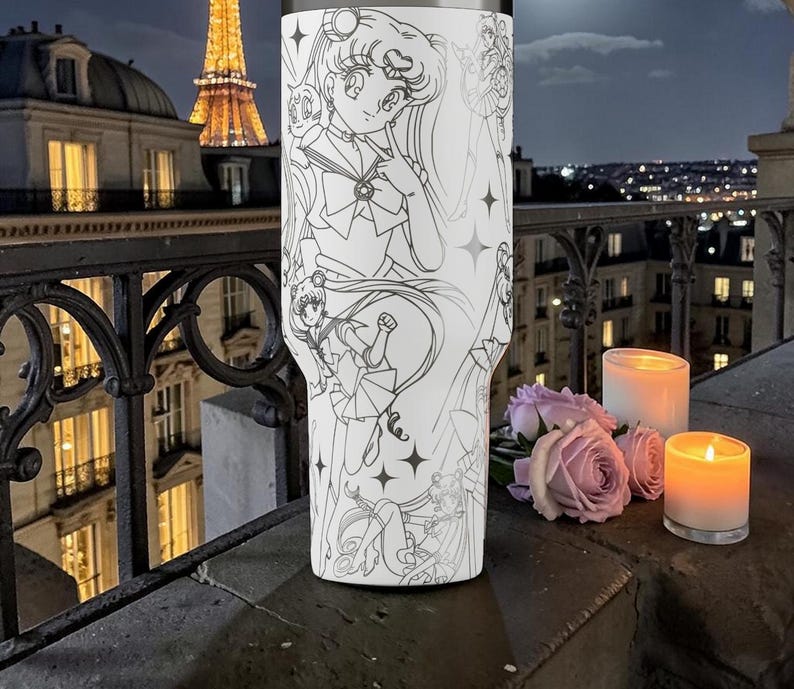 May include: A white tumbler with a black and white manga illustration. The design features a character, stars, and other figures. The tumbler is set against a night cityscape with lit buildings and candles, creating a romantic atmosphere.