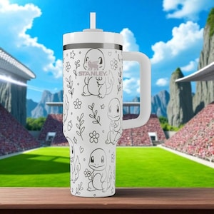 Puede incluir: Vaso Stanley blanco con asa y pajita, con un diseño de Charmander en blanco y negro. El vaso tiene el logotipo de Stanley y está sobre un fondo de estadio.