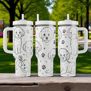 May include: White insulated tumbler with a handle, featuring a repeating pattern of cartoon dog illustrations, paw prints, and stars. The tumbler has a white lid and a straw. The brand name "STANLEY" is visible on one of the tumblers.