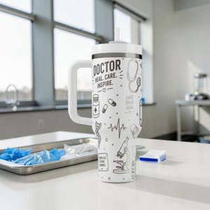 May include: White insulated tumbler with a handle and a straw. The tumbler is decorated with black line art of medical symbols, including a stethoscope, pills, and a DNA strand. Text on the tumbler reads "DOCTOR HEAL. CARE. INSPIRE."