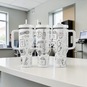May include: Three white insulated tumblers with black line art illustrations of paramedic symbols, including an ambulance, AED, and stethoscope. Each tumbler has a white handle and lid with a straw. The text "PARAMEDIC" is on one tumbler.