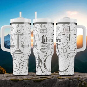 May include: Three white stainless steel tumblers with handles and straws, featuring black line art of Libra zodiac symbols, scales, stars, moons, and text including "Libra," "Charming," "Romantic," "Diplomatic," "Tactful," "Clever," and "Fair."
