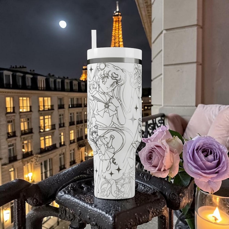 May include: White tumbler with a black and white anime design featuring a character with long hair and a sailor uniform. The tumbler has a white lid and a straw. The background includes a night scene with the Eiffel Tower and a full moon.