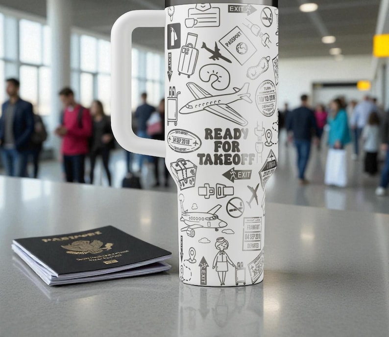 May include: A white travel mug with a large handle, decorated with black and white travel-themed illustrations, such as aeroplanes and passport stamps. The text "READY FOR TAKEOFF" is visible. A passport is placed next to the mug.