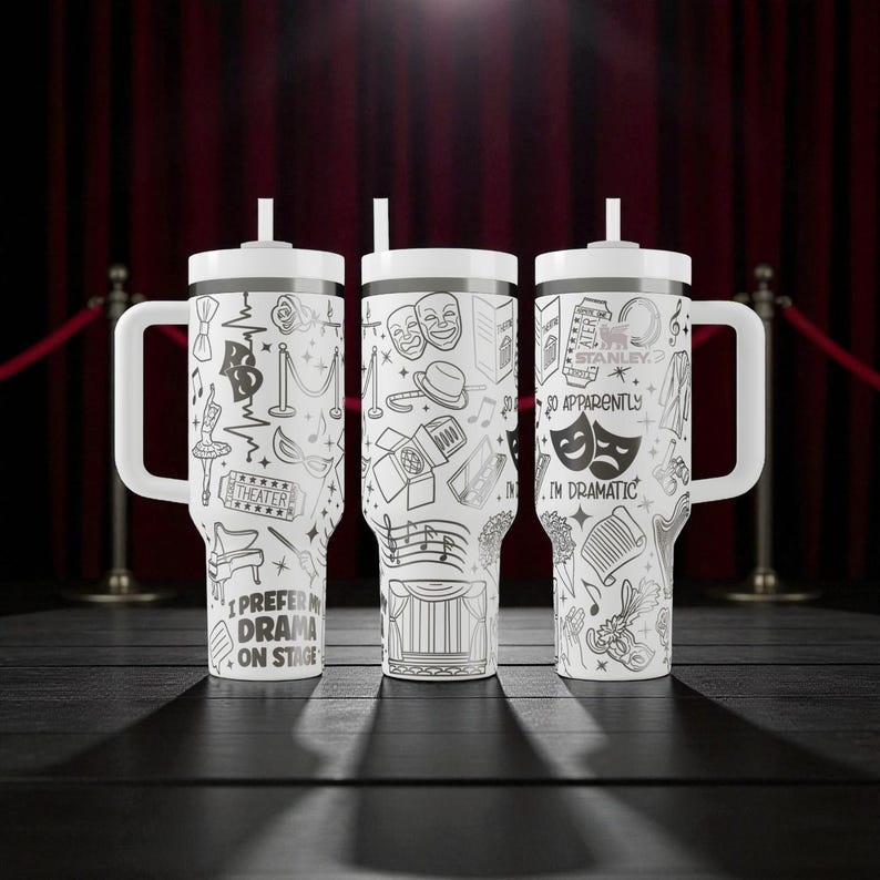 May include: Three white travel mugs with black line art of theater-related images and text. Each mug has a white handle, lid, and straw. The text on the mugs includes "I PREFER DRAMA ON STAGE" and "I'M DRAMATIC".