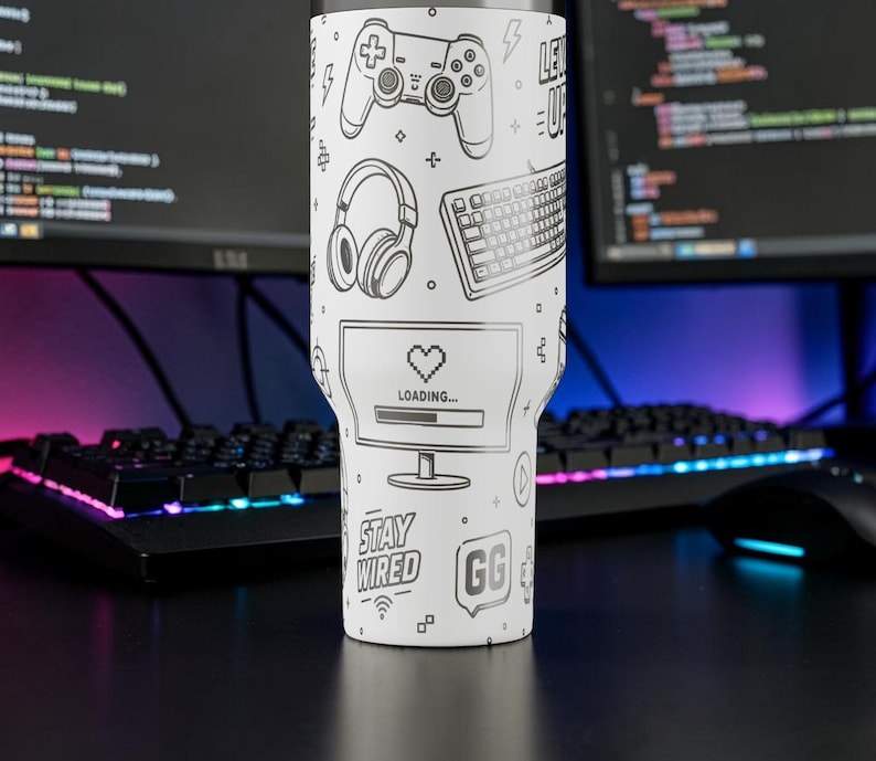 May include: White tumbler with black line art of gaming-related icons, including a controller, headphones, keyboard, and a computer screen with a loading bar. The text "Stay Wired" and "GG" are also featured.