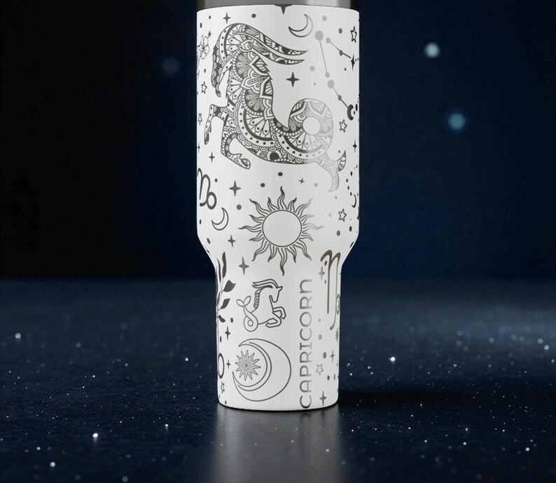 K&ouml;nnte beinhalten: Wei&szlig;er Becher mit einem schwarzen Capricorn-Tierkreiszeichen-Design, einschlie&szlig;lich Sterne, Monde und Sonnen. Das Wort "CAPRICORN" ist vertikal aufgedruckt. Der Becher hat einen Edelstahlrand und einen wei&szlig;en K&ouml;rper.
