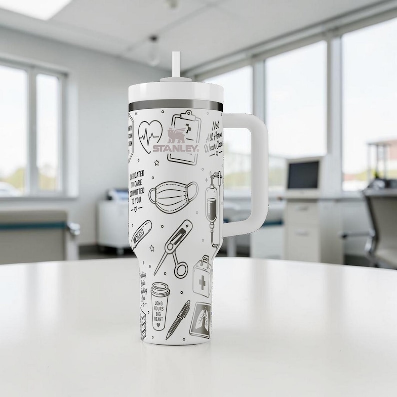 May include: White Stanley tumbler with a black and white medical-themed design. The design includes a heart rate monitor, medical mask, and IV drip. The tumbler has a white handle and a straw.
