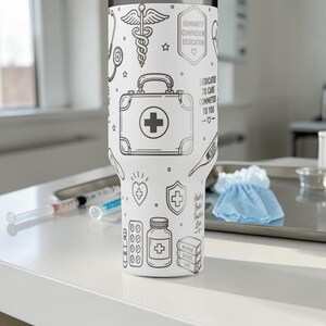 May include: White insulated tumbler with black line art of medical symbols, including a first aid kit, pills, and a thermometer. The tumbler has text that reads "HUMANITY COMPASSION DEDICATION" and "DEDICATED TO CARE COMMIT TO YOU".