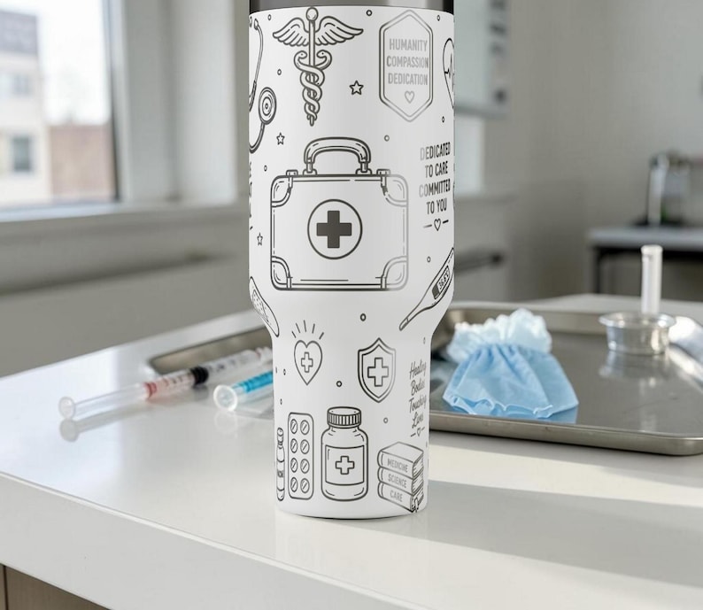 May include: White insulated tumbler with black line art of medical symbols, including a first aid kit, pills, and a thermometer. The tumbler has text that reads "HUMANITY COMPASSION DEDICATION" and "DEDICATED TO CARE COMMIT TO YOU".