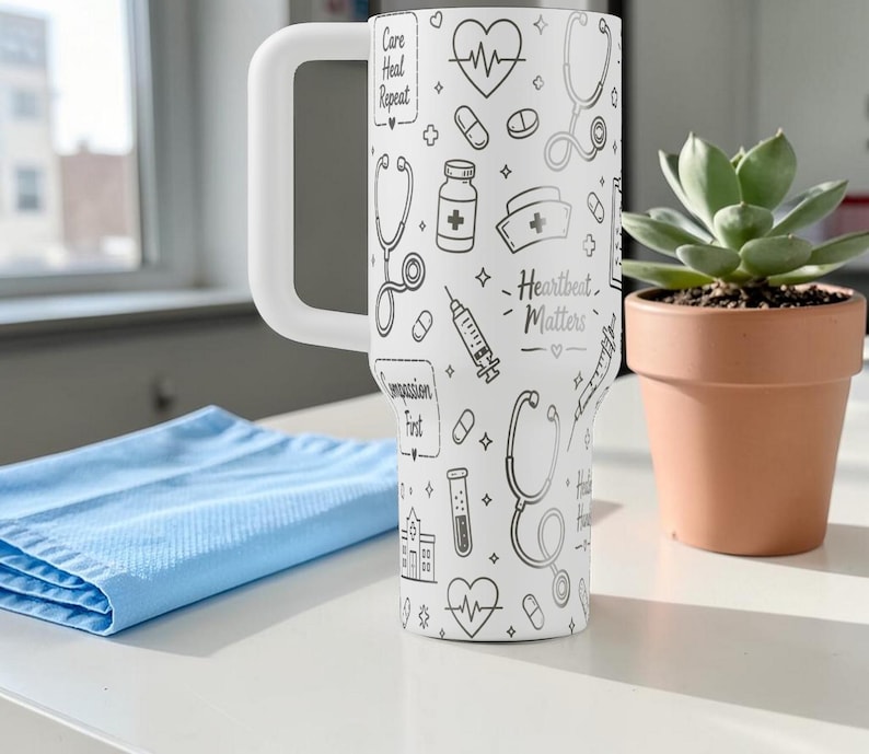 Puede incluir: Un vaso blanco con un asa blanca grande, decorado con ilustraciones de tem&aacute;tica m&eacute;dica en negro. El vaso presenta estetoscopios, pastillas y el texto "Heartbeat Matters". Un pa&ntilde;o azul y una suculenta en maceta est&aacute;n en el fondo.