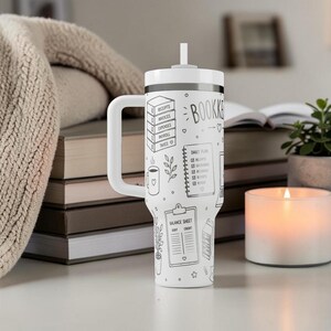 Puede incluir: Vaso blanco con asa y pajita, con ilustraciones en negro de elementos de contabilidad. El dise&ntilde;o incluye la palabra "BOOKKEEPER", recibos, facturas y un plan diario. Una vela y una peque&ntilde;a planta est&aacute;n en el fondo.