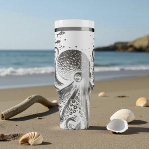 May include: White travel mug with a black and white octopus design. The tumbler features a detailed illustration of an octopus with its tentacles and suckers, along with fish and dots. The mug has a white lid and a silver band.