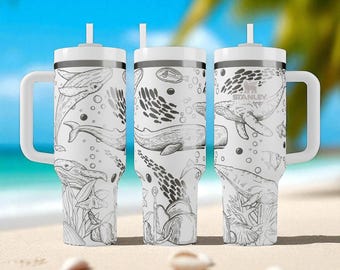 May include: Three white stainless steel tumblers with handles and straws, each featuring a black line art pattern of whales, fish, and coral. The Stanley brand logo is visible on the right tumbler, which is set against a blurred beach background.