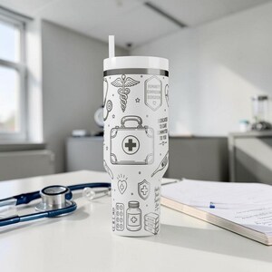 May include: White tumbler with a black and white medical-themed design. The tumbler features illustrations of medical tools, a first aid kit, and text that reads "Humanity, Compassion, Dedication, Dedicated to Care, Committed to You". Includes a white straw.