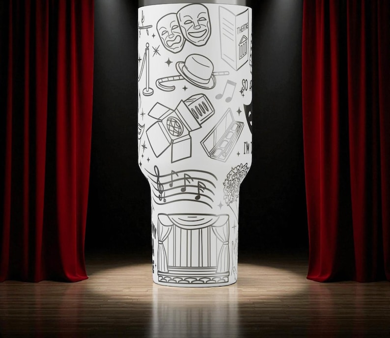 May include: A white tumbler with a black line drawing of theater-related elements, including masks, a stage, musical notes, and a spotlight. The tumbler is cylindrical with a slightly tapered base. The background features red curtains and a wooden stage.