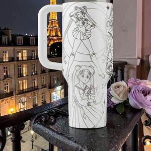 May include: White tumbler with a large handle, featuring a detailed black and white illustration of anime characters. The design includes multiple figures in various poses. The background shows a city at night.