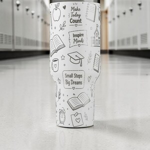 May include: White tumbler with black line art illustrations and text. The design includes an apple, books, a coffee cup, a graduation cap, and the phrases "Make Today Count," "Inspire Minds," and "Small Steps Big Dreams."