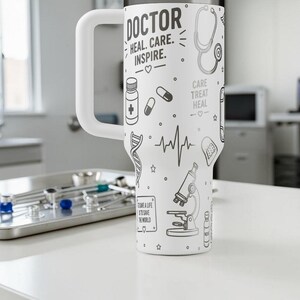 May include: White tumbler with a large white handle, decorated with medical-themed illustrations in black. The tumbler features the words "DOCTOR, HEAL, CARE, INSPIRE" and other medical symbols like a stethoscope and pills.