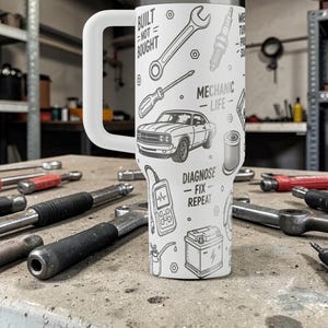 May include: White insulated tumbler with a large handle, featuring a black and white mechanic-themed design. The design includes tools, a classic car, and the phrases "Built Not Bought" and "Diagnose Fix Repeat."