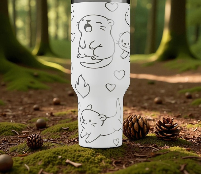 K&ouml;nnte beinhalten: Wei&szlig;er Becher mit einem sich wiederholenden Muster aus Cartoon-Ottern, Herzen und Flammen in Schwarz. Der Becher ist zylindrisch und scheint aus Edelstahl zu sein. Der Hintergrund ist ein Waldboden mit Moos, Tannenzapfen und Eicheln.