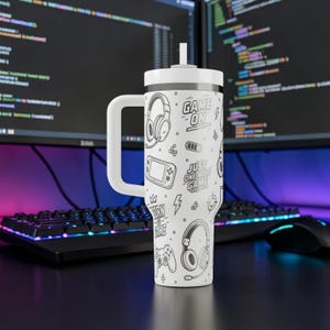 May include: White insulated tumbler with a handle and straw, featuring a black and white gaming-themed design. The design includes headphones, game controllers, and the phrases "Game On" and "Just One More Game."