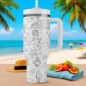 Puede incluir: Vaso Stanley blanco con asa, decorado con criaturas marinas como medusas, estrellas de mar y tortugas. El vaso tiene tapa y pajita blancas. El fondo muestra una escena de playa con palmeras y naranjas en rodajas.