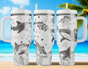 May include: Three white stainless steel tumblers with handles and straws, featuring a black and white line art pattern of whale sharks, schools of fish, bubbles, and seashells. The Stanley logo is printed on the rightmost tumbler.