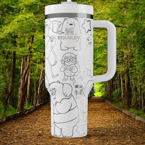 May include: White Stanley tumbler with a handle, featuring black and white cartoon character illustrations. The tumbler has a white lid and a black band. The background shows a path through a forest.