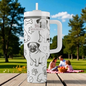 May include: A white Stanley tumbler with a handle and straw, featuring a repeating black and white pattern of pug dogs, paw prints, bones, and hearts. The Stanley logo is printed in the center of the cup among the dog illustrations.