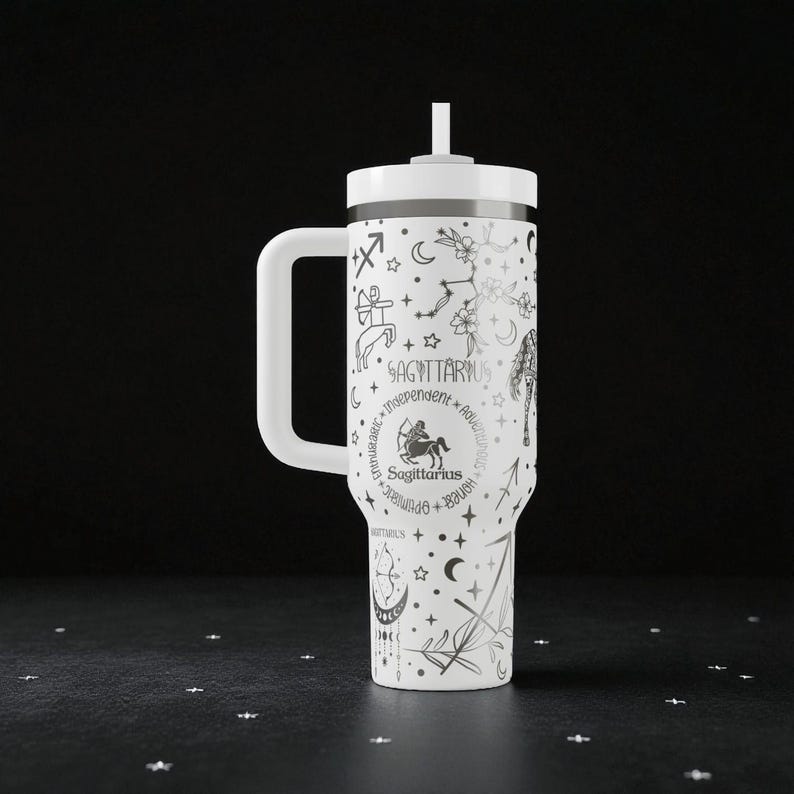 Op de afbeelding: Witte beker met een handvat en een rietje, met een Boogschutter sterrenbeeld ontwerp. Het ontwerp bevat sterrenbeelden, sterren en het woord "Boogschutter". De beker is ontworpen voor koude dranken.