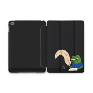 Puede incluir: Funda negra para iPad con una imagen de dibujos animados de una rana verde escribiendo con una pluma. La rana lleva una camisa azul. La funda está abierta, revelando la pantalla del iPad a la izquierda.