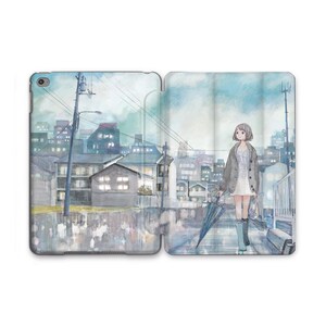 Puede incluir: Una funda para tableta con una ilustración en acuarela de una persona caminando bajo la lluvia. La obra de arte representa un paisaje urbano con edificios y una persona sosteniendo un paraguas. La paleta de colores incluye tonos de azul, gris y blanco.