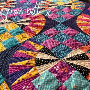 May include: A colorful quilt with a variety of patterns and colors, including pink, purple, yellow, blue, and green. The quilt is made up of squares and circles, and the stitching is visible. The quilt has the text "love from beth x" written on it.