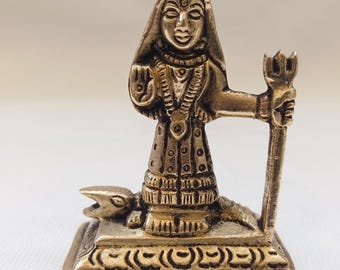 May include: A small gold-colored metal statue of a deity standing on a snake. The deity is holding a trident in their right hand and has a third eye on their forehead.