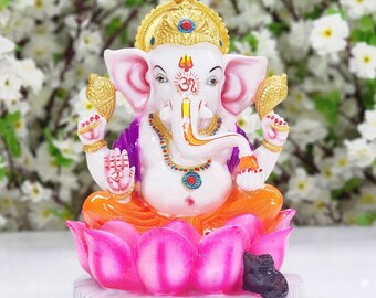 May include: A white Ganesha statue with a gold crown and a pink lotus base. The statue is sitting on a white base with a black mouse at the bottom.